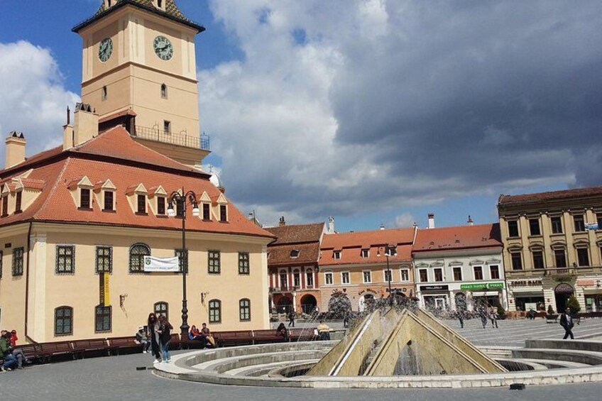 A historic square with a prominent clock tower, a fountain, and traditional buildings. 4