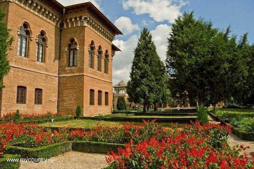 A brick building with arched windows, surrounded by a well-manicured garden with red flowers and green hedges. 5