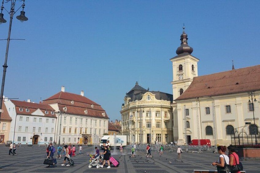A public square with historic buildings, a clock tower, and people walking. 4