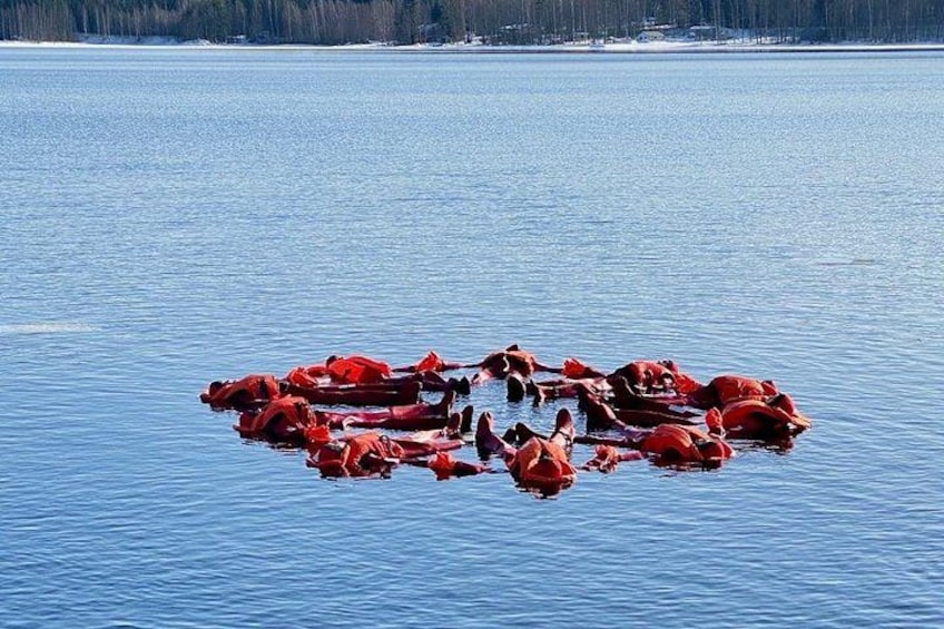 A circular arrangement of red boats on a calm lake with a forested shoreline in the background. 3
