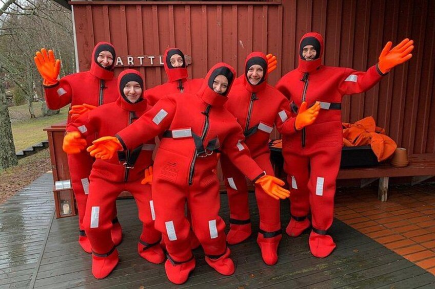 A group of people in red suits with orange gloves posing in front of a wooden structure. 5