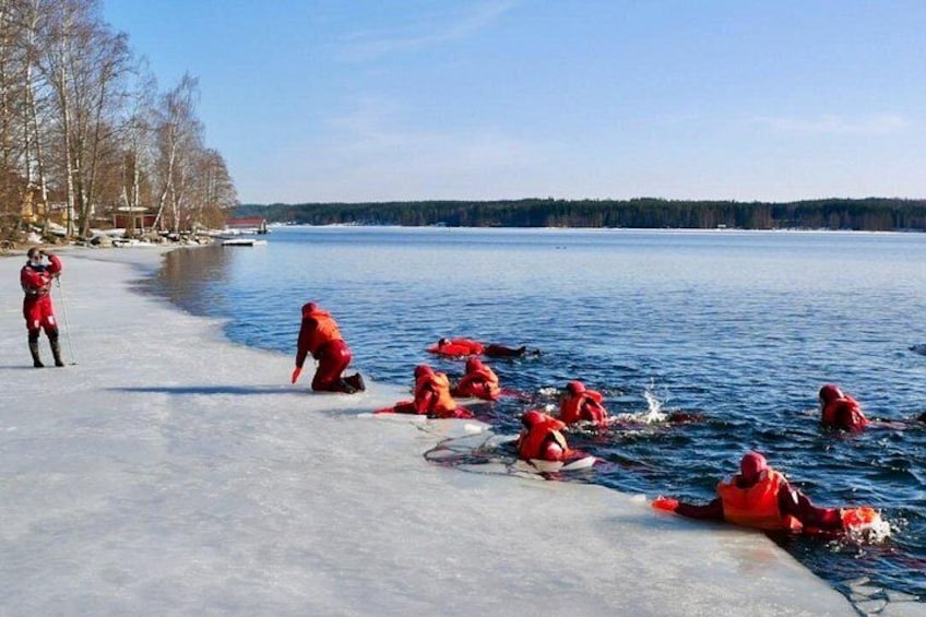 People in red jackets ice fishing on a frozen lake with trees and a clear sky in the background. 2