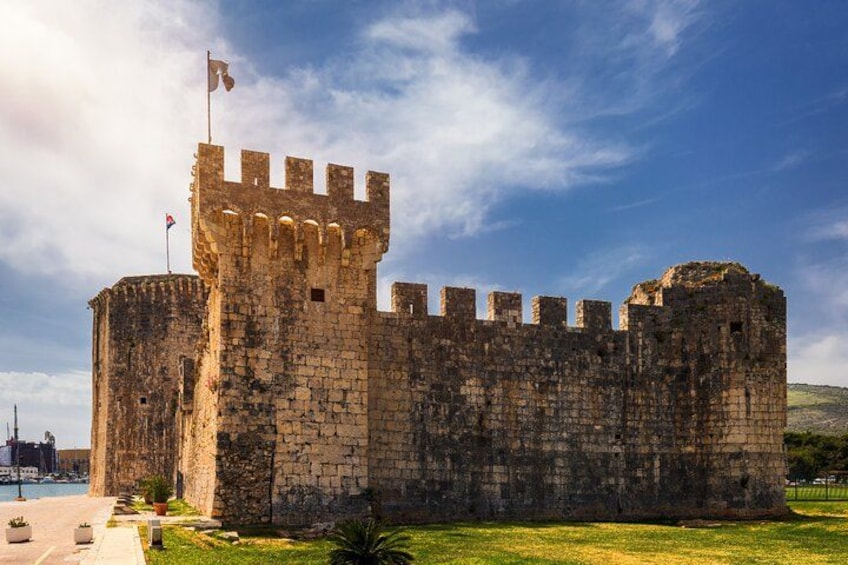 A historic stone castle with a flag on top, surrounded by a grassy area. 3