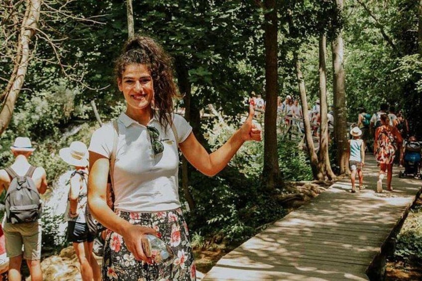 A person in a white shirt and floral skirt walking on a wooden boardwalk in a forested area. 4