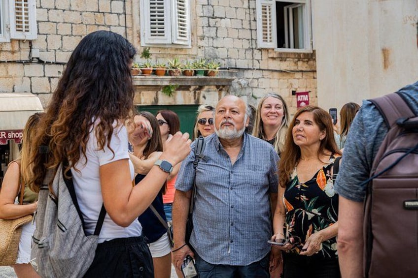 A group of people standing on a street with stone buildings and a shop sign. 5