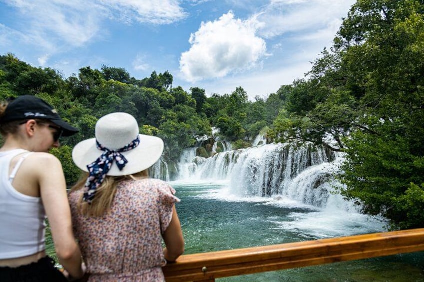 A waterfall with lush greenery and a wooden railing. 4