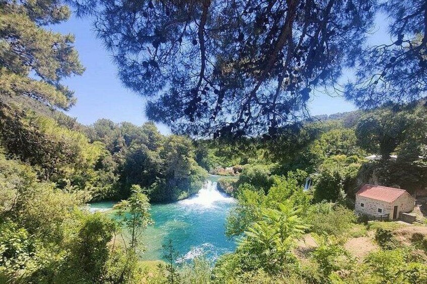 A turquoise lake surrounded by dense greenery and a small stone building. 3