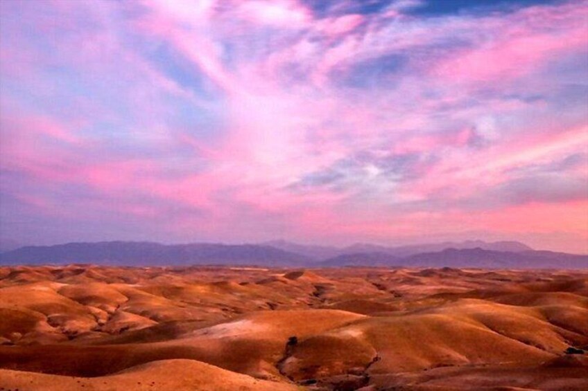 A desert landscape with rolling hills and a pink and purple sky. 2