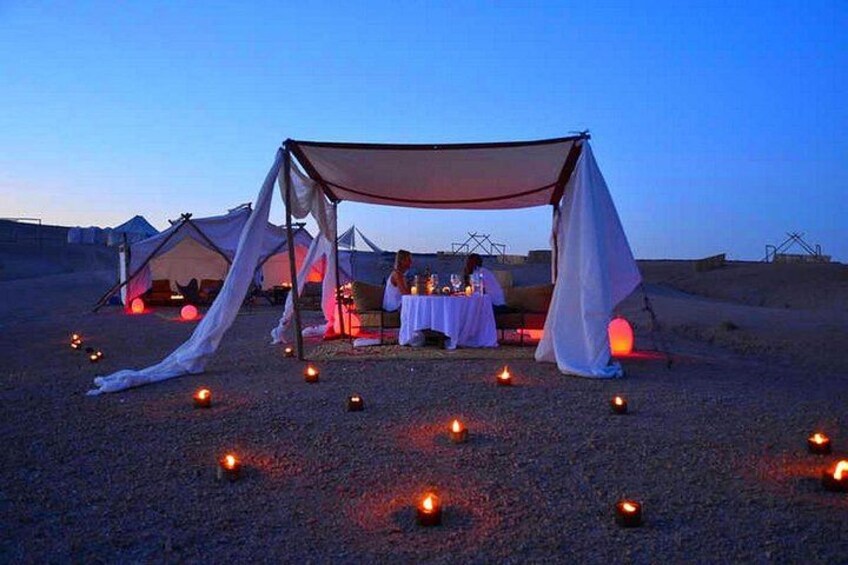 Tienda de campaña en el desierto con una mesa dispuesta para una comida, rodeada de velas. 1