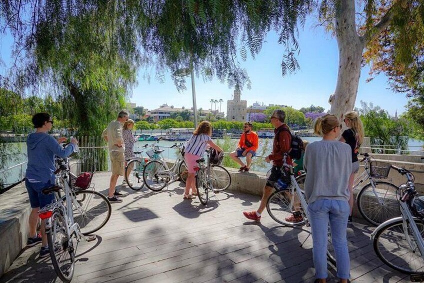People on a wooden boardwalk near a body of water, with bicycles and trees in the background. 3