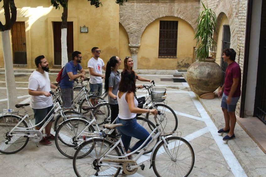En grupp människor står runt cyklar på en innergård, med en byggnad i bakgrunden. 4