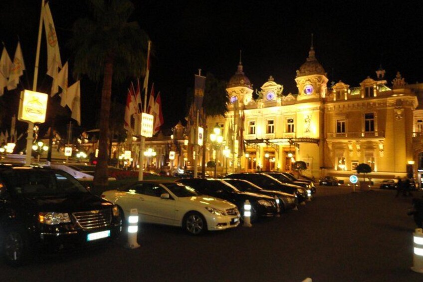 A nighttime street with parked cars and a grand building with domed architecture. 1