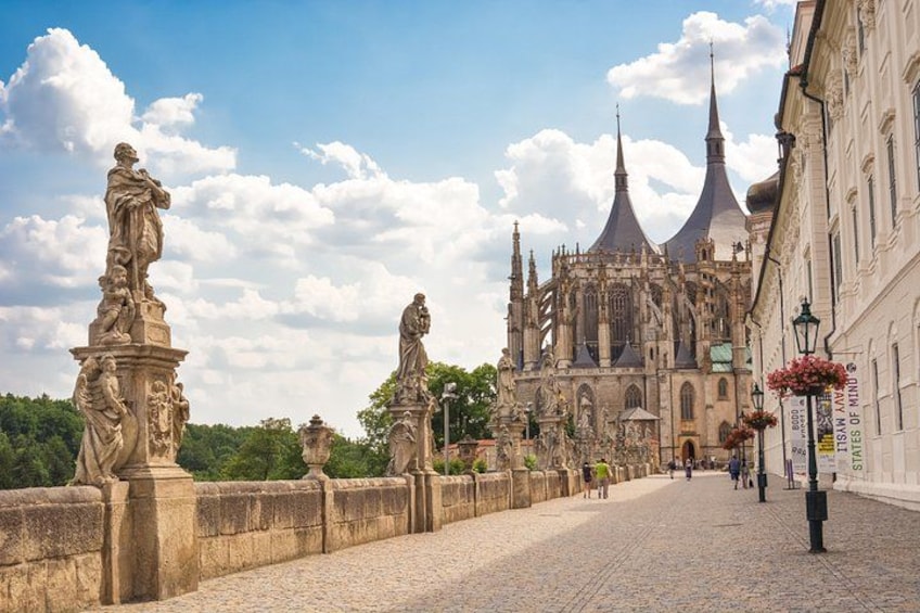 A cobblestone bridge with statues, a cathedral with spires, and a clear sky. 4