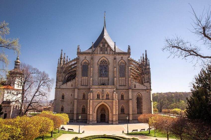 Una gran catedral de estilo gótico con una aguja destacada, rodeada de jardines cuidados y un cielo despejado. 1