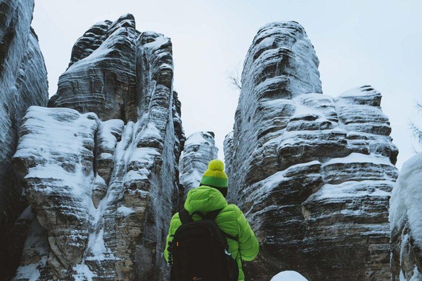 Une personne portant une veste verte et un chapeau jaune escalade une formation rocheuse recouverte de neige. 3