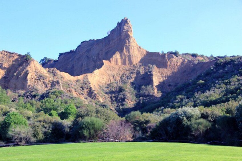 A mountain with a prominent peak, a green field in the foreground, and sparse vegetation on the slopes. 3