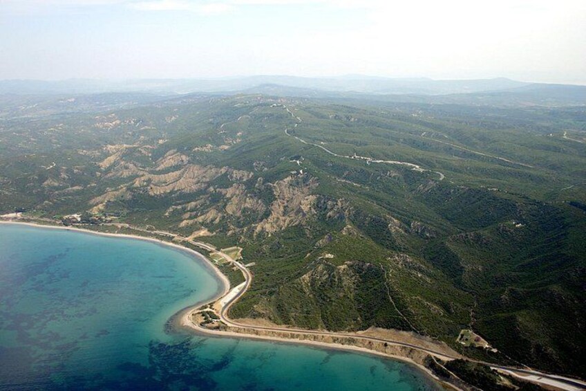 A coastal landscape with a winding road, dense forest, and a large body of water. 4