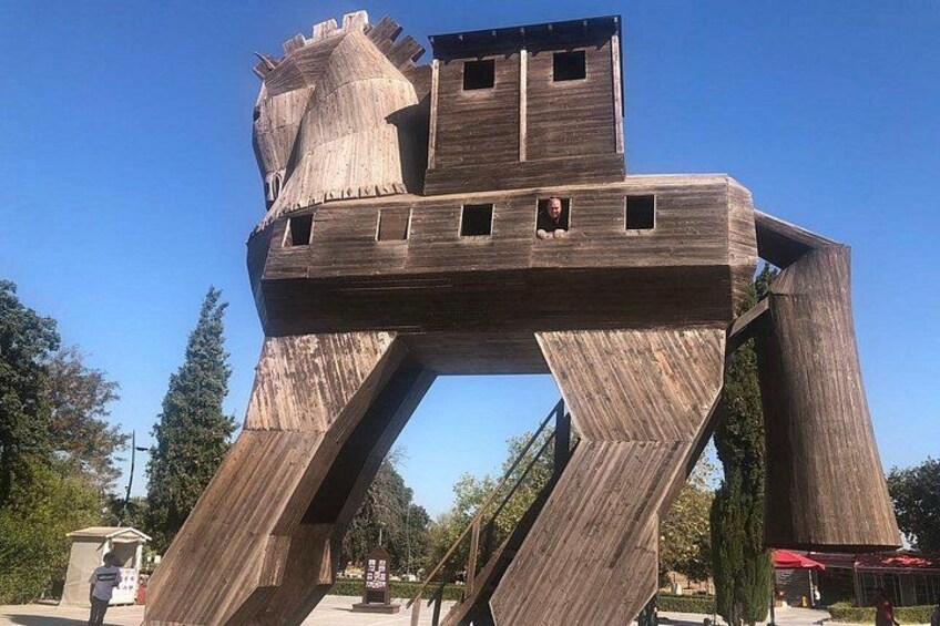 A large wooden sculpture resembling a horse with a rider, set in an outdoor area with trees and a clear sky. 5
