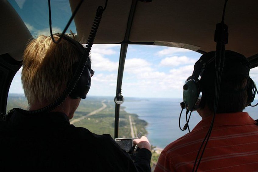 To personer i en helikoptercockpit, hvoraf den ene har headset på, og den anden holder et kamera. 5