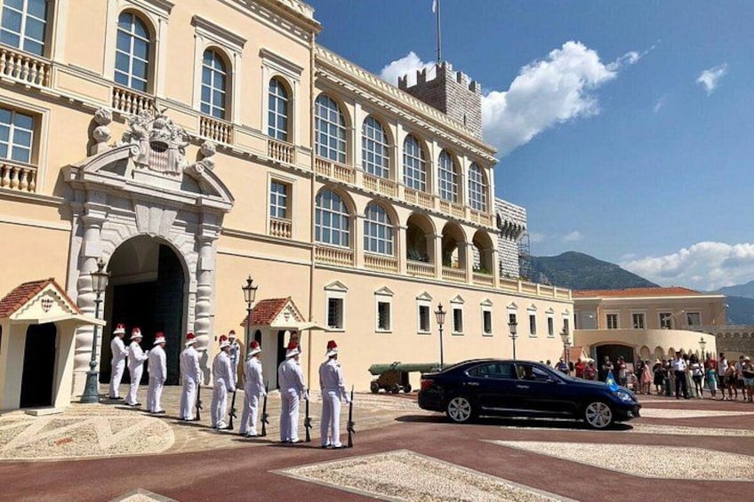 En byggnad med en stor valvöppning, en grupp personer i uniform som står framför den, och en bil som är parkerad i närheten. 2
