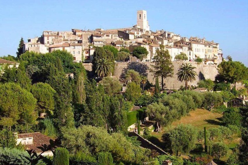 Un pueblo en la ladera con edificios históricos, una torre destacada y abundante vegetación. 1