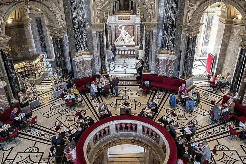 Un gran salón con suelos de mármol, asientos rojos y una estatua central. 2