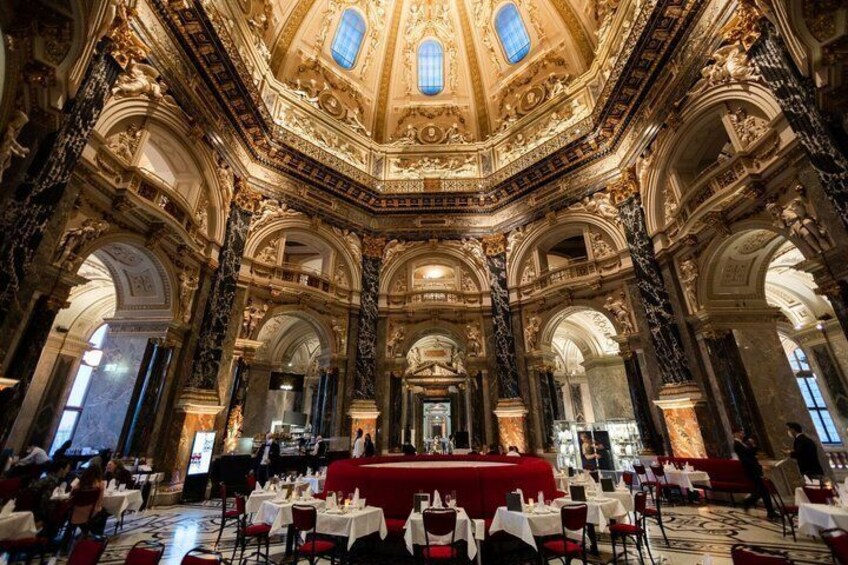 Un salón comedor ornamentado con techos altos, detalles intrincados en oro y manteles rojos. 5