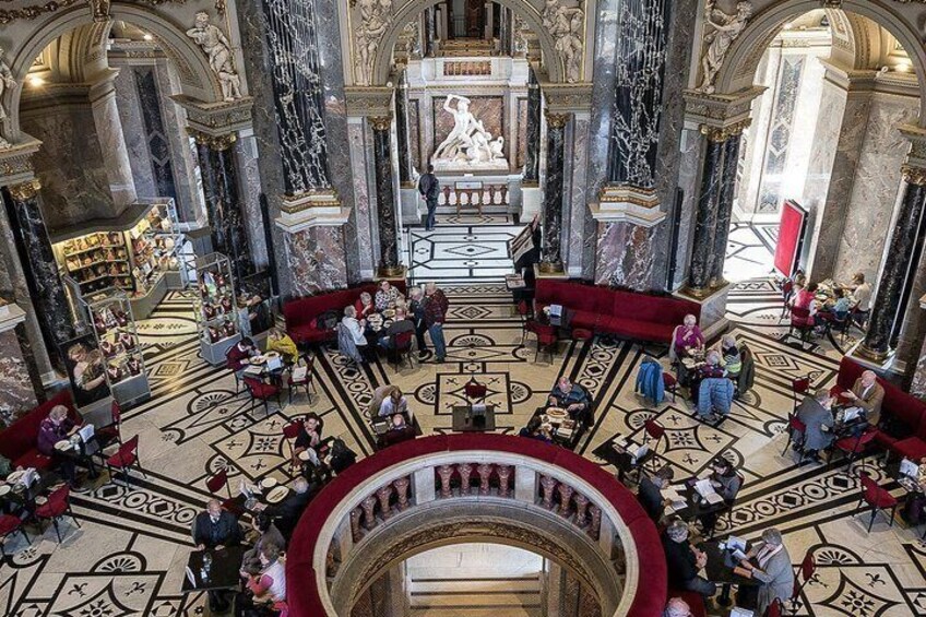 Un gran salón con suelos de mármol, asientos rojos y una estatua central. 2