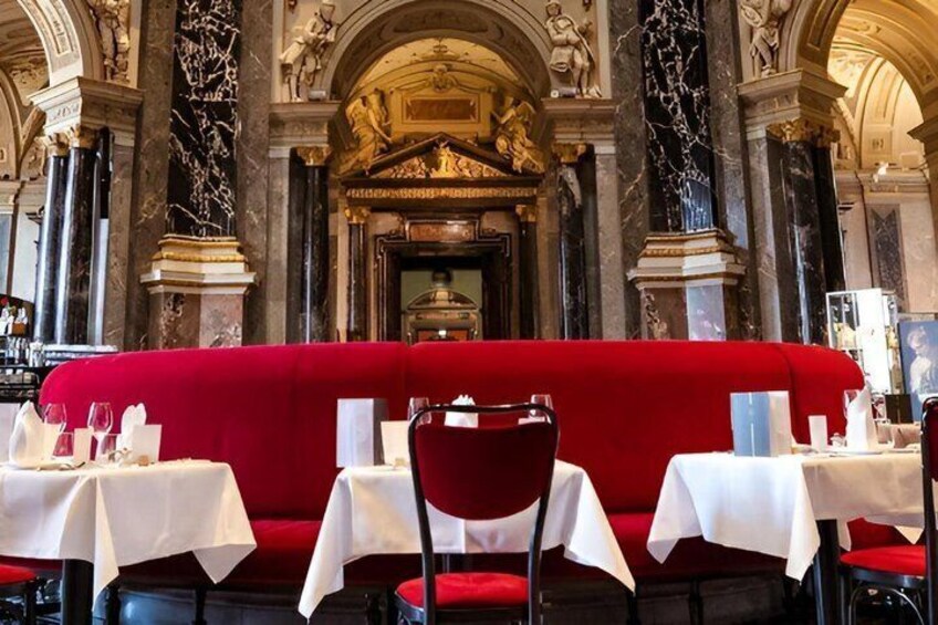 Un banco tapizado rojo con manteles blancos y sillas en un edificio histórico con columnas de mármol y decoraciones ornamentales. 4