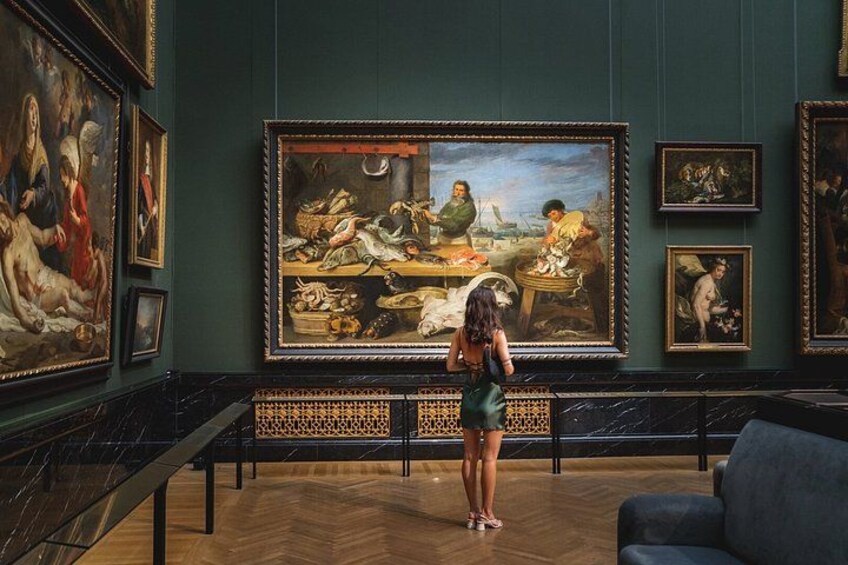Interior de un museo con un cuadro grande de una escena de mercado en la pared, piso de mármol y un sofá azul. 5