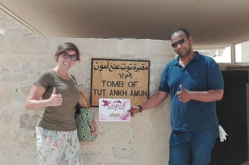 Due persone in piedi di fronte a un muro con un cartello che recita 'TOMB OF TUT ANKH AMUN' e il logo di 'Egypt Travel'. 4