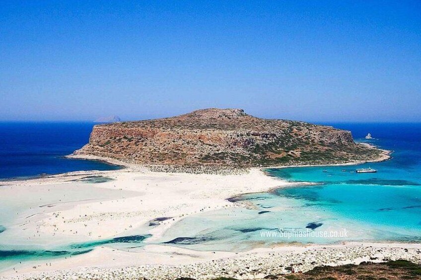 Eine Küstenlandschaft mit einer markanten Felseninsel, klarem türkisfarbenem Wasser und einem Sandstrand. 2