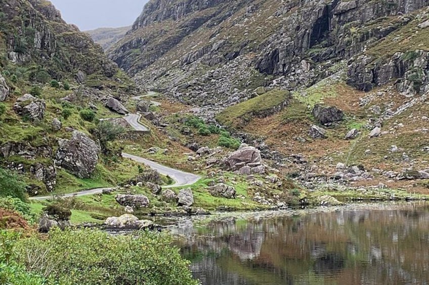 A winding mountain road, rocky terrain, and a calm lake. 2