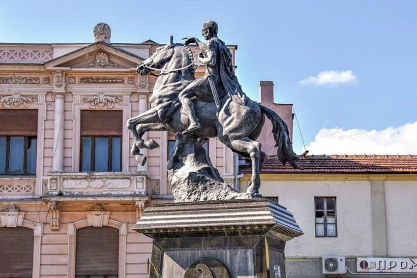 Une statue représentant une personne à cheval, placée devant un bâtiment à l’architecture classique. 1