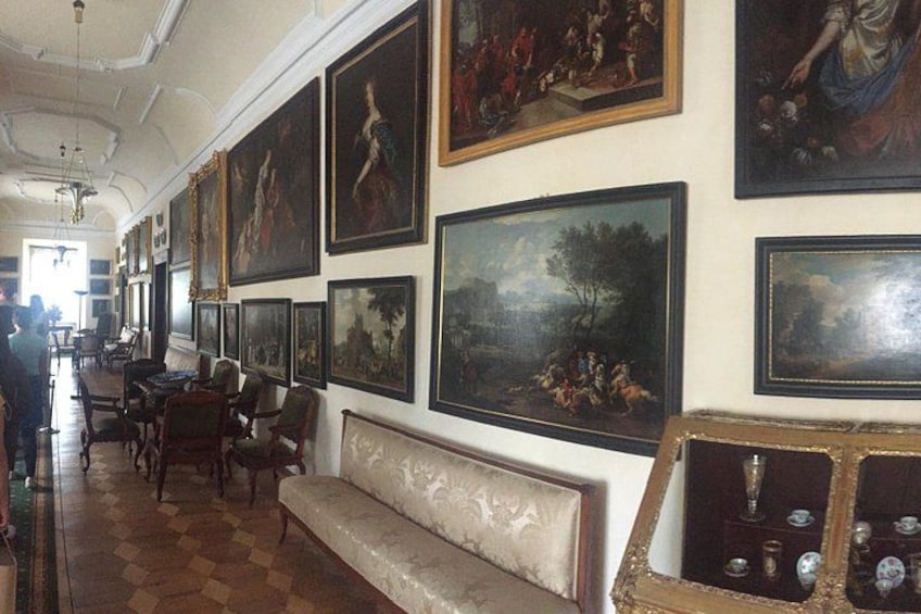 Eine Galerie mit klassischen Gemälden an den Wänden, einem Holzboden und einer Sitzbank. 4