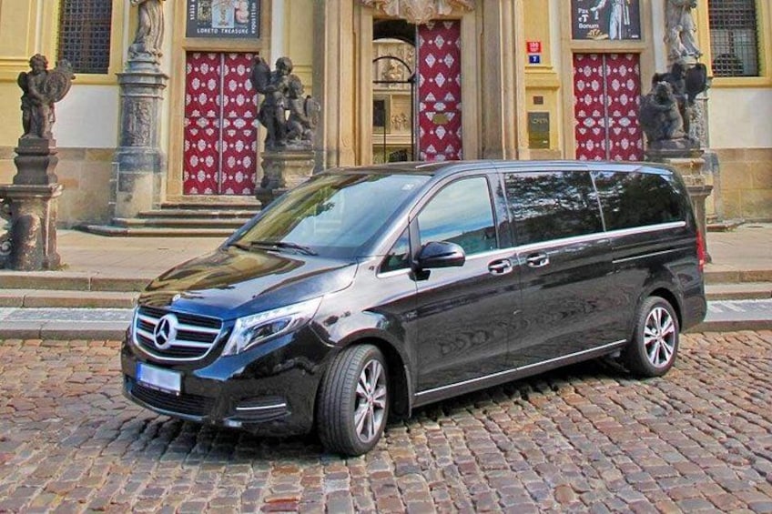 Ein schwarzer Mercedes-Benz Minivan steht auf einer Kopfsteinpflasterstraße vor einem Gebäude mit roten Türen und Statuen. 2