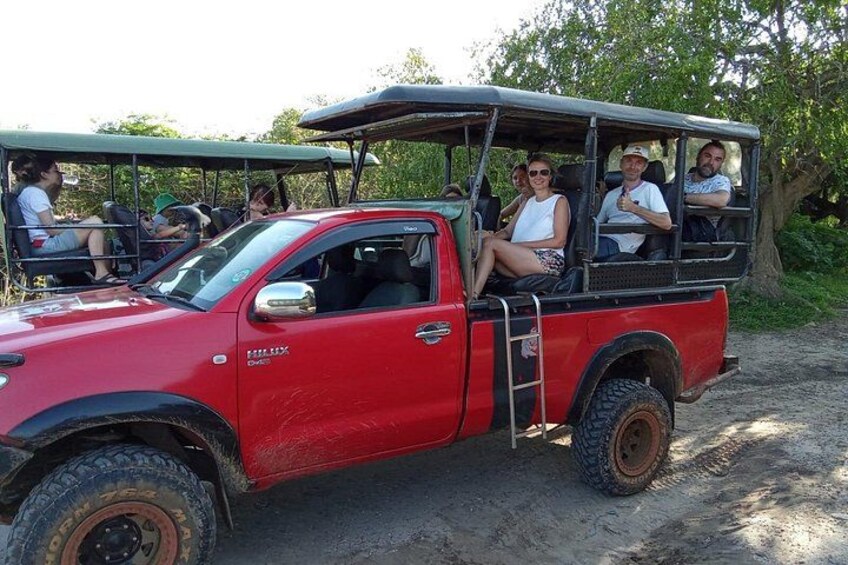 Una camioneta roja con pasajeros estacionada en un camino de tierra. 5