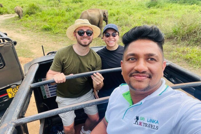 A safari vehicle with three people, a grassy field, and elephants in the background. 2