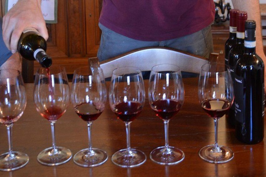 A person pouring wine into several glasses on a wooden table. 4
