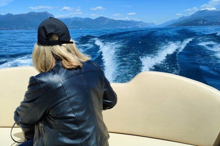 A person in a black leather jacket and cap on a boat, with a mountainous landscape in the background. 4