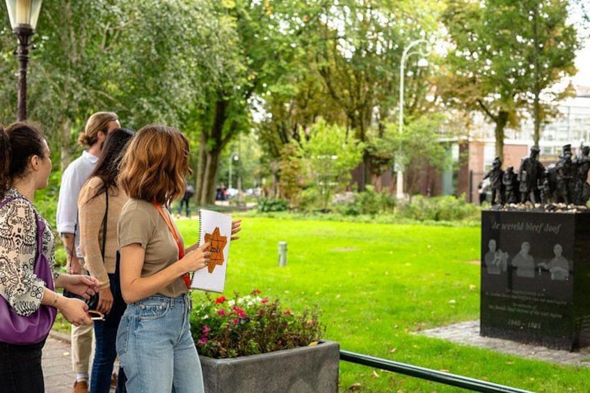 A group of people standing in a park, looking at a memorial with a plaque and statues. 2
