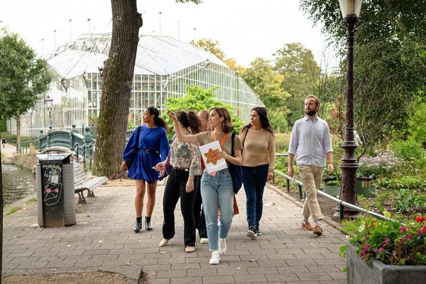 A group of people walking on a paved path in a park with a glass greenhouse structure in the background. 3
