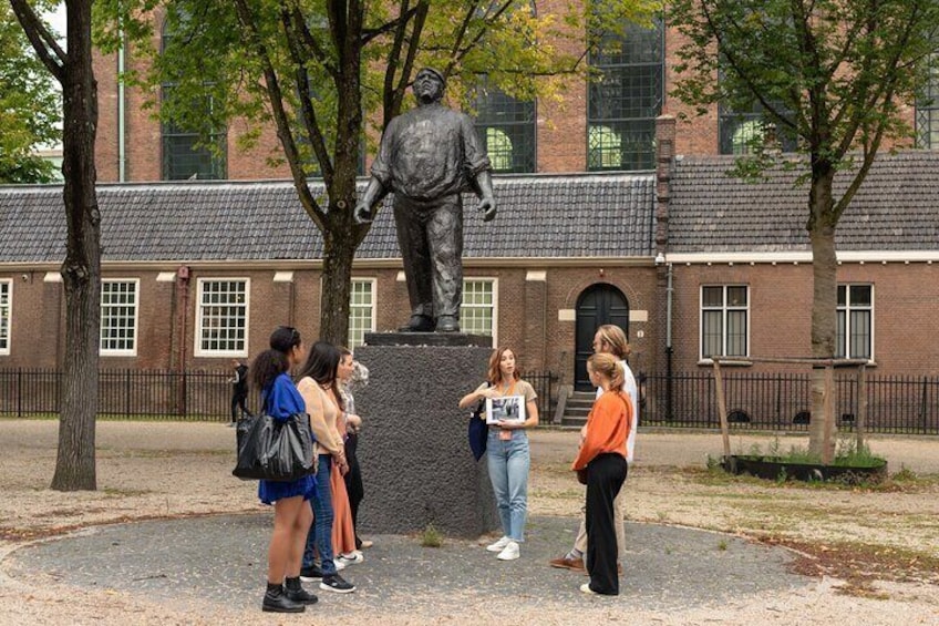 A statue of a man on a pedestal in a park with a brick building in the background. 3