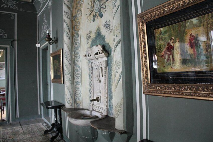 A room with a vintage toilet, a framed painting, and a patterned wallpaper. 3