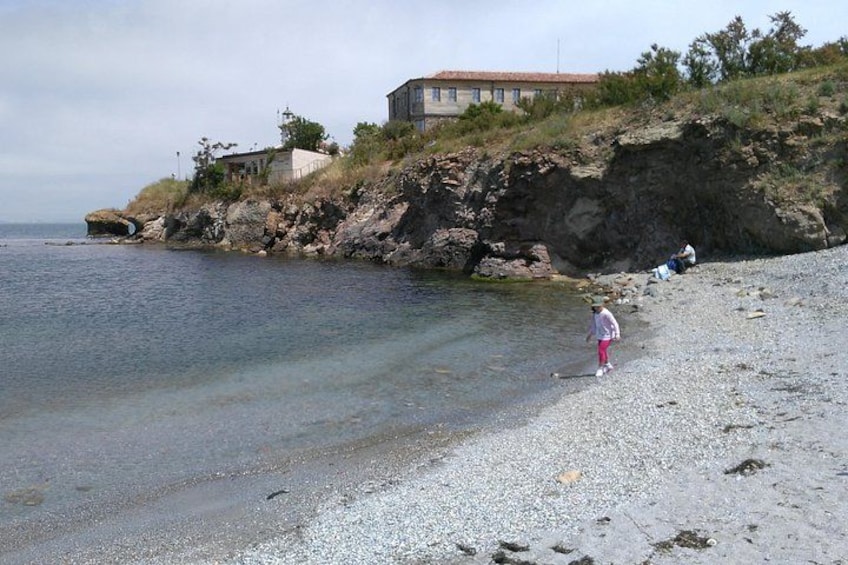 A rocky shoreline with clear water, a person standing, and a building on a hill. 3