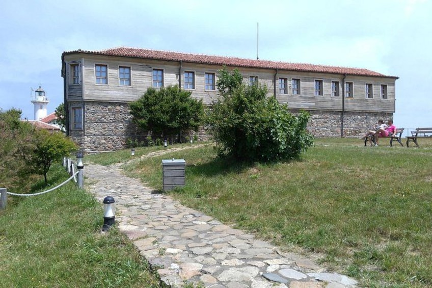 A stone pathway leading to a historic building with a red-tiled roof, surrounded by grass and trees. 4