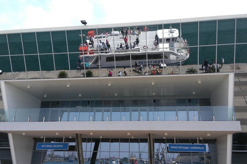 A modern building with a glass facade and a boat docked at its top. 2
