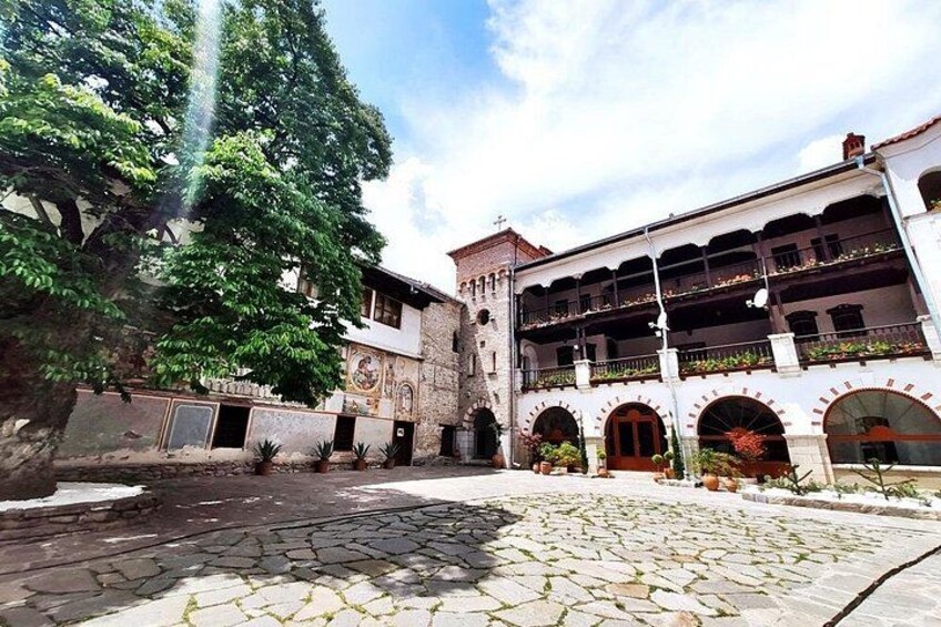 Un patio con adoquines de piedra, un árbol y un edificio con múltiples balcones y arcos. 2