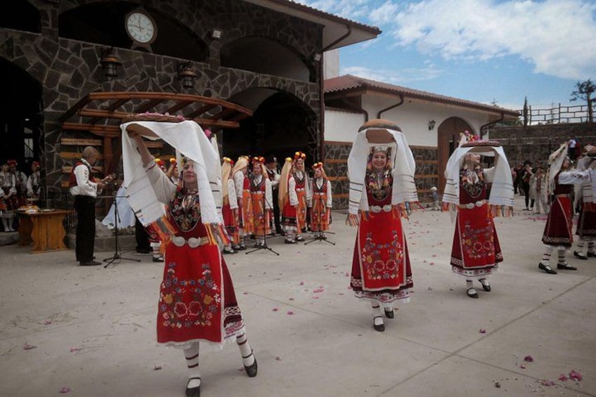A group of people in traditional red and white attire performing a dance in an outdoor setting with stone buildings in the background. 5