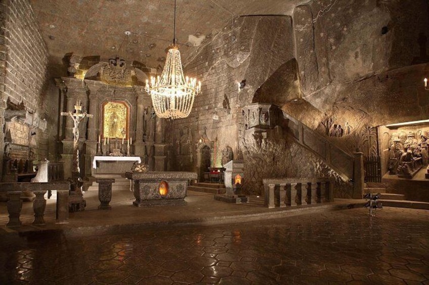 An ancient church interior with a large chandelier, altar, and stone walls. 1